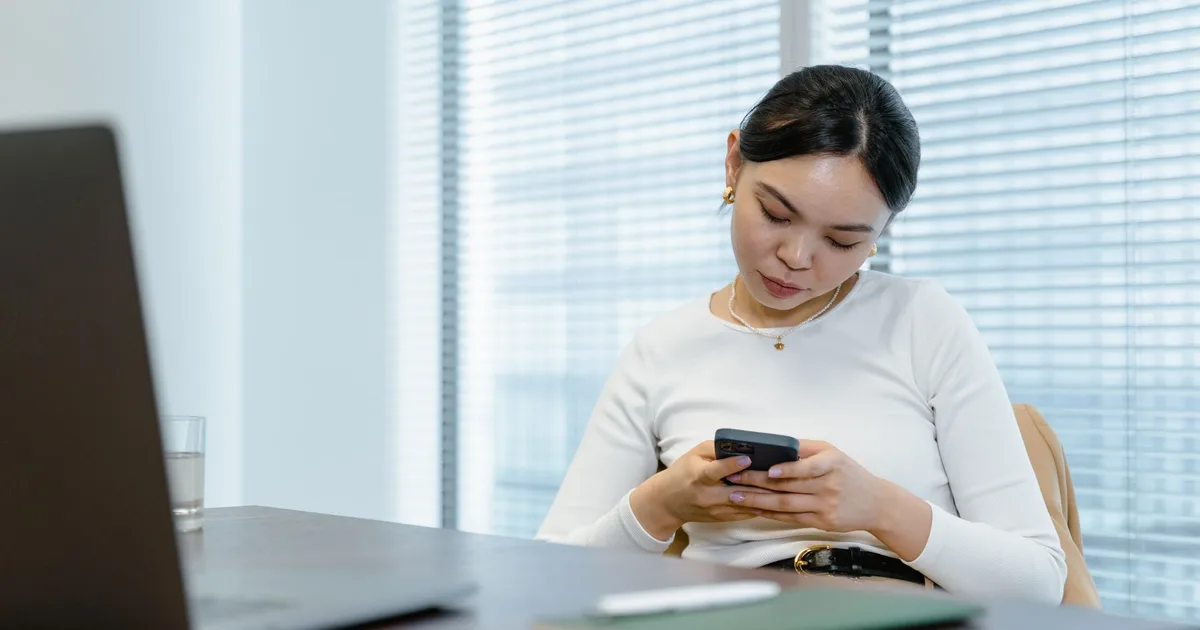 Profissional respondendo clientes pelo celular no escritório, com o notebook aberto ao lado